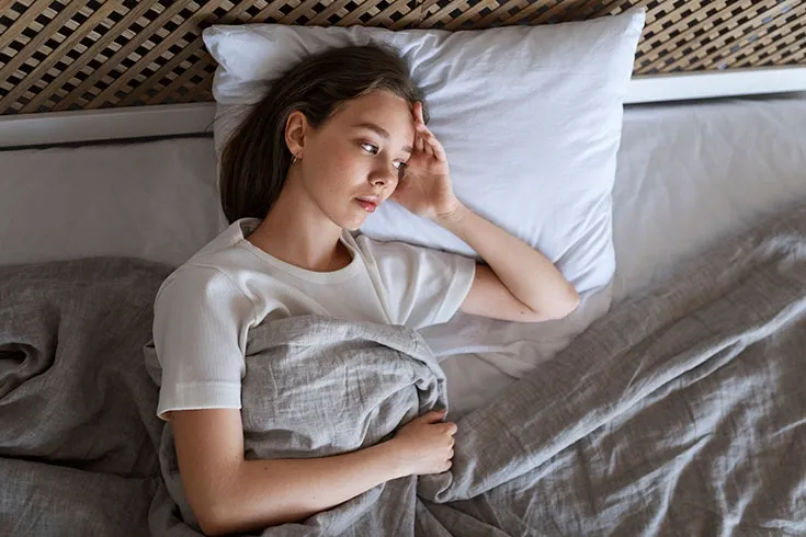Mulher deitada na cama com uma express&atilde;o preocupada