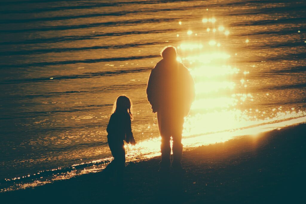 Silhueta de criança e adulto lado a lado em praia. A imagem simboliza lembranças de vidas passadas e deja vu