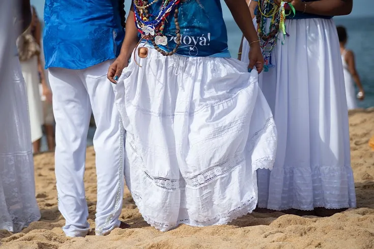 Pessoas descal&ccedil;as na praia, vestidas de branco e azul, celebrando Iemanj&aacute;
