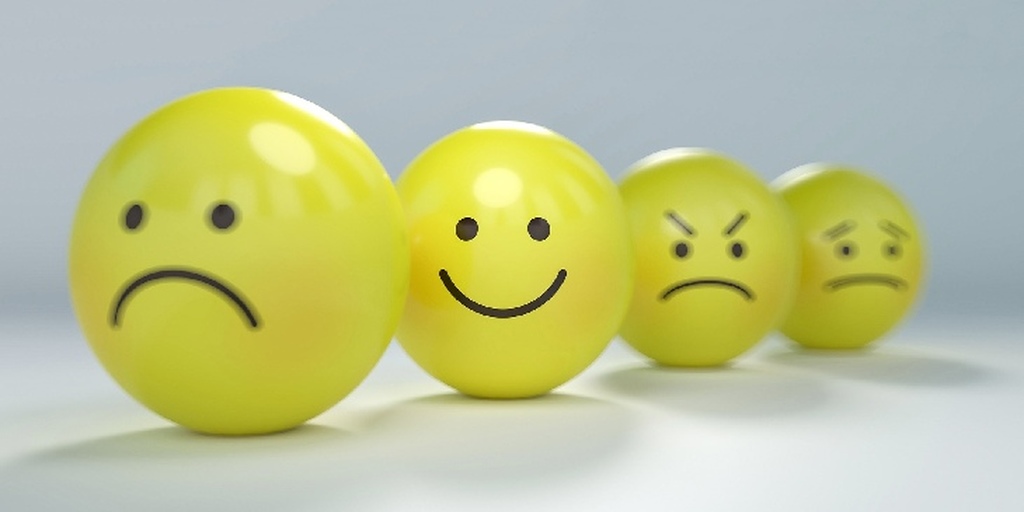 4 bolinhas amarelas, similares a emojis, cada uma com uma expressão (tristeza, raiva, medo), mas a que está em foco é o sorriso, que representa afirmações positivas