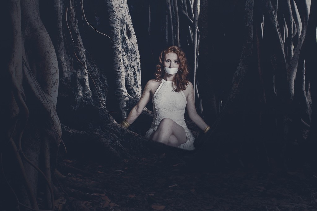 Mulher amordaçada no escuro entre árvores, simbolizando sonhar com sequestro