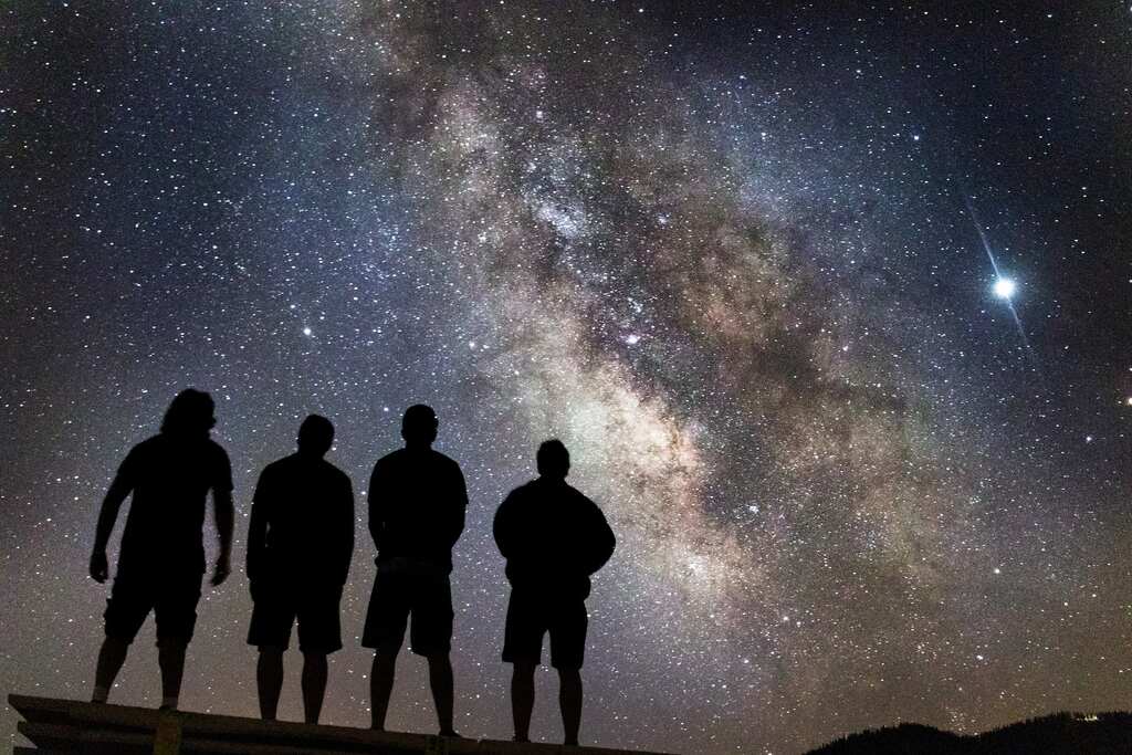 Silhueta de quatro pessoas olhando para o céu, que exibe muitas estrelas e astros de luz, simbolizando a terapia multidimensional