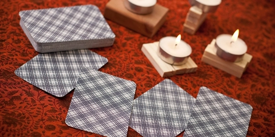 Mesa com velas de rechaud, toalha vermelha e algumas cartas ainda viradas.