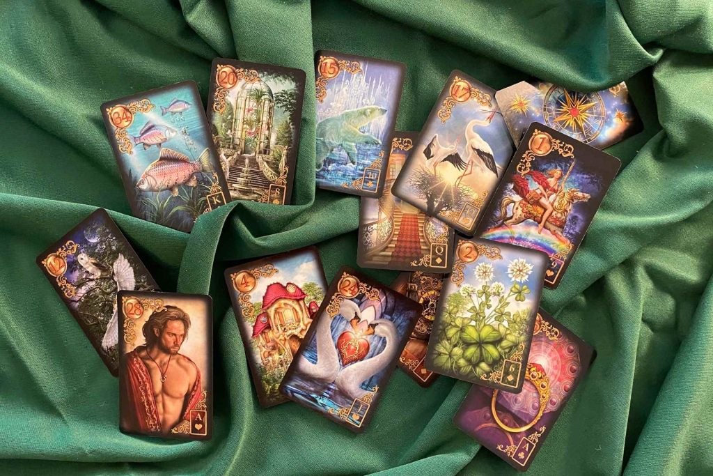 Cartas do baralho cigano aleatoriamente dispostas sobre toalha verde.