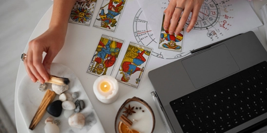 Vista de cima da mesa de uma Especialista Astrocentro, com um laptop, cartas de Tarot, velas, incensos e cristais.