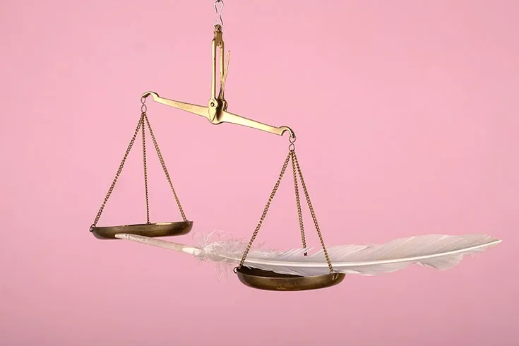 Balança sobre fundo rosa, com uma pena branca movendo uma das pás