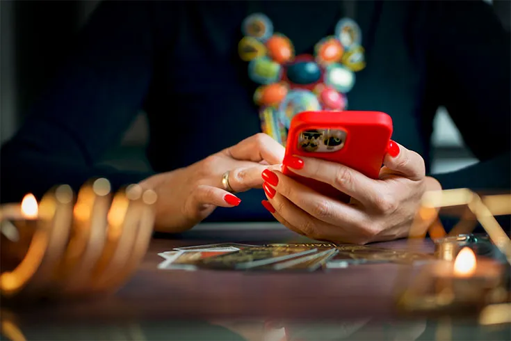 Taróloga fazendo atendimento pelo seu celular, enquanto tira as cartas na mesa