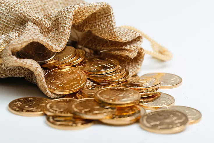 Saco de pano, aberto, com moedas de ouro dentro, se esparramando pela mesa.
