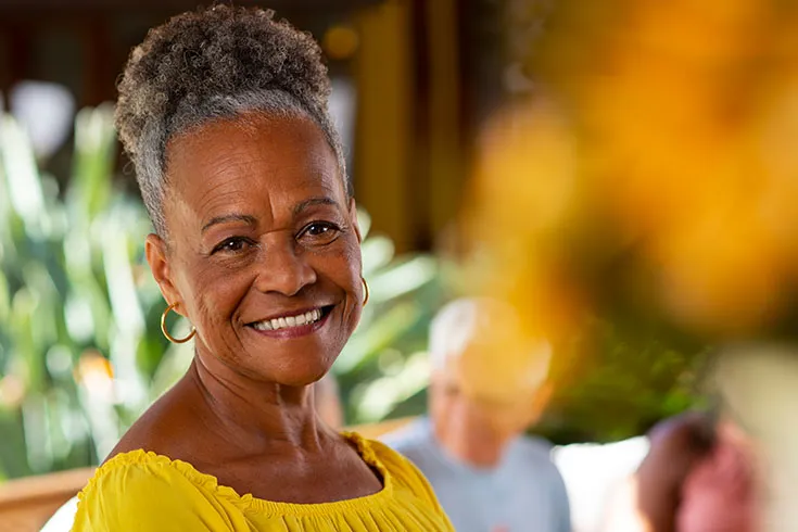 Mulher madura, de amarelo, cabelo preso e sorridente