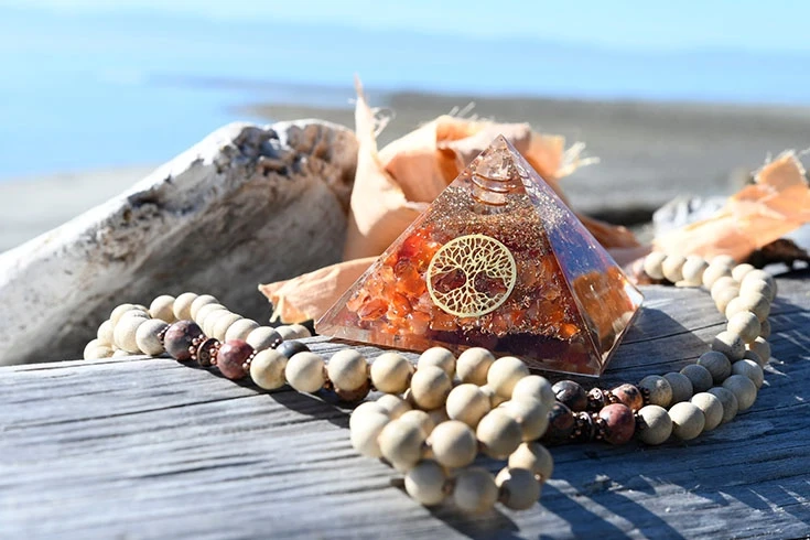 Orgonite exposto sobre mesa de madeira, na praia, com colar de contas