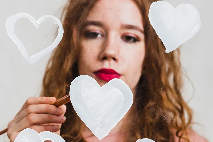 Mulher pensativa, desenhando corações brancos em um espelho