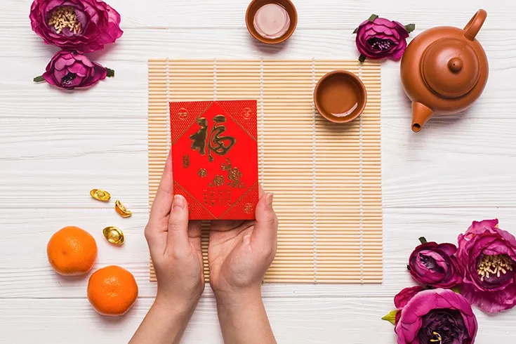 Duas m&atilde;os segurando uma pequena caixa vermelha com escritas em mandarim