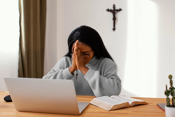 Jovem em momento de oração ou segurando um terço próximo a um notebook (simbolizando a fé na era digital)