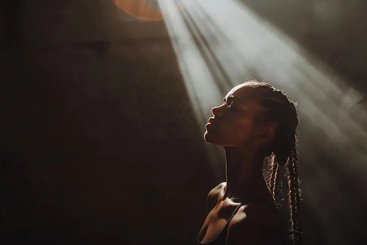 Uma mulher no escuro contemplando os raios de sol que adentram o lugar