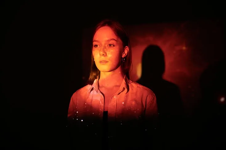 Mulher com uma express&atilde;o de preocupa&ccedil;&atilde;o enquanto uma luz alaranjada ilumina o seu rosto