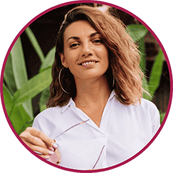 Imagem da cliente é uma mulher jovem sorridente com cabelo castanho ondulado, usando blusa branca e brincos em argola, em fotografia de perfil circular.